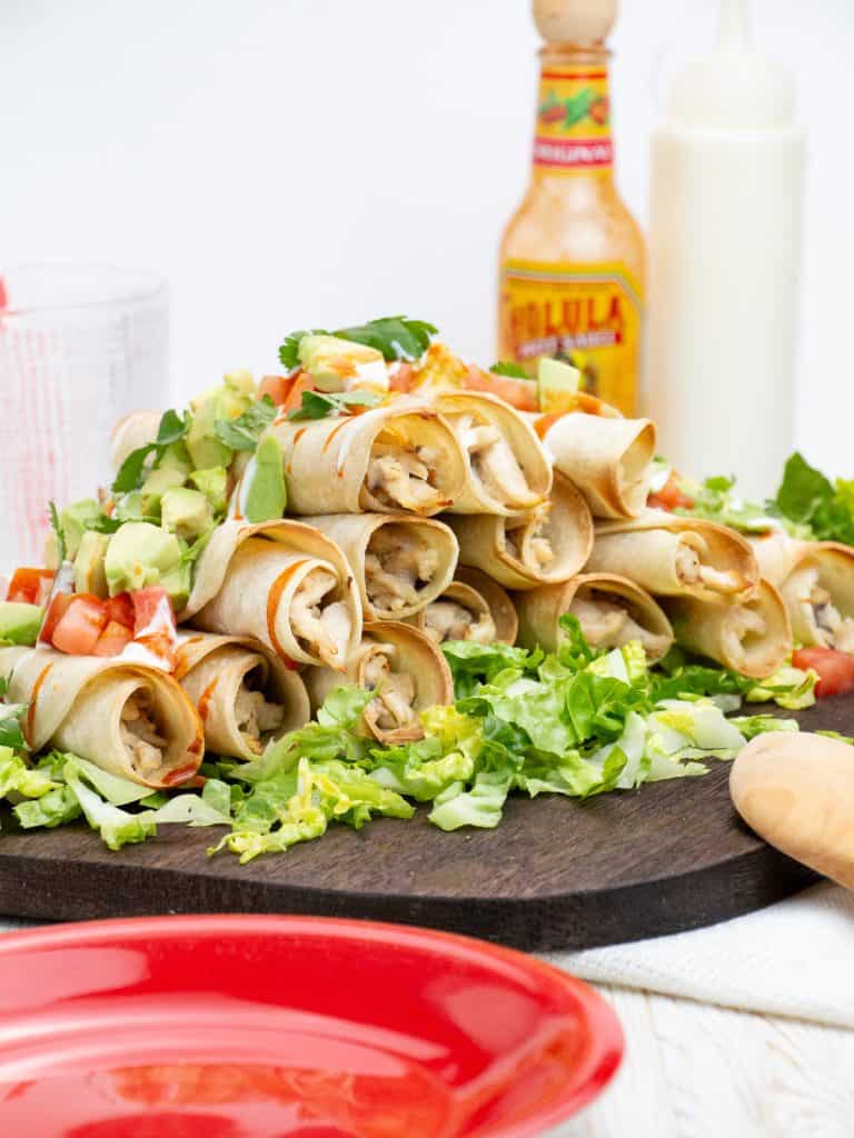 baked chicken flautas with toppings of avocado, tomato and sour cream