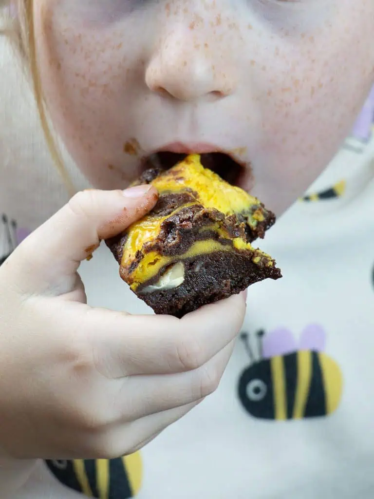 a kid biting into a piece of pumpkin cheesecake brownie